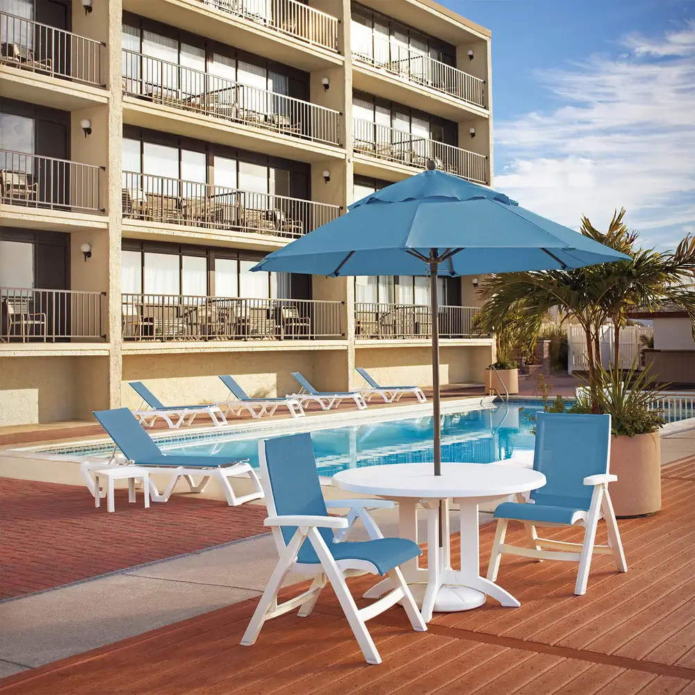 Hotel pool deck featuring Sky Blue Jamaica Beach dining chairs and a matching chaises shaded by a large commercial umbrella.
